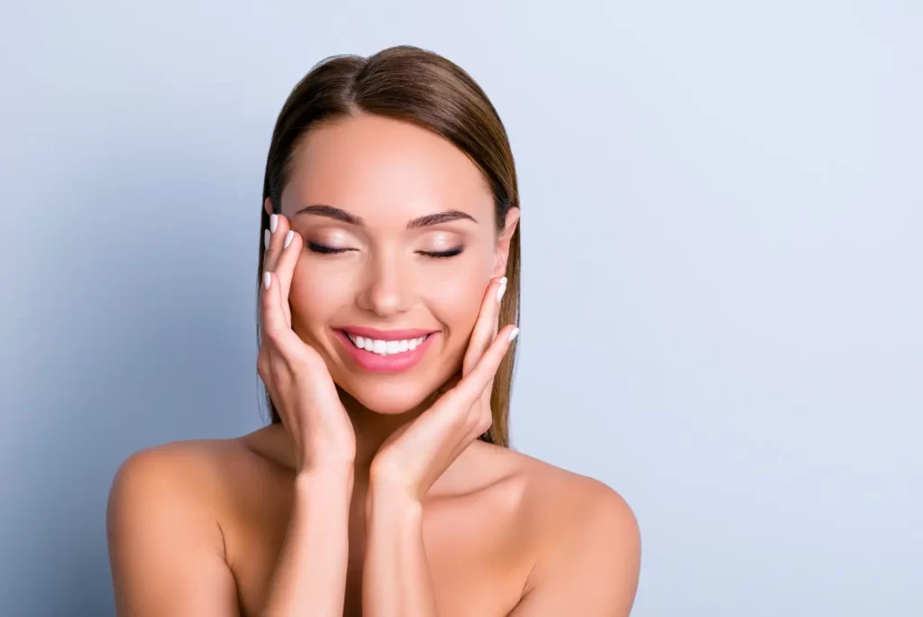 Woman smiling with eyes closed while touching her smooth facial skin