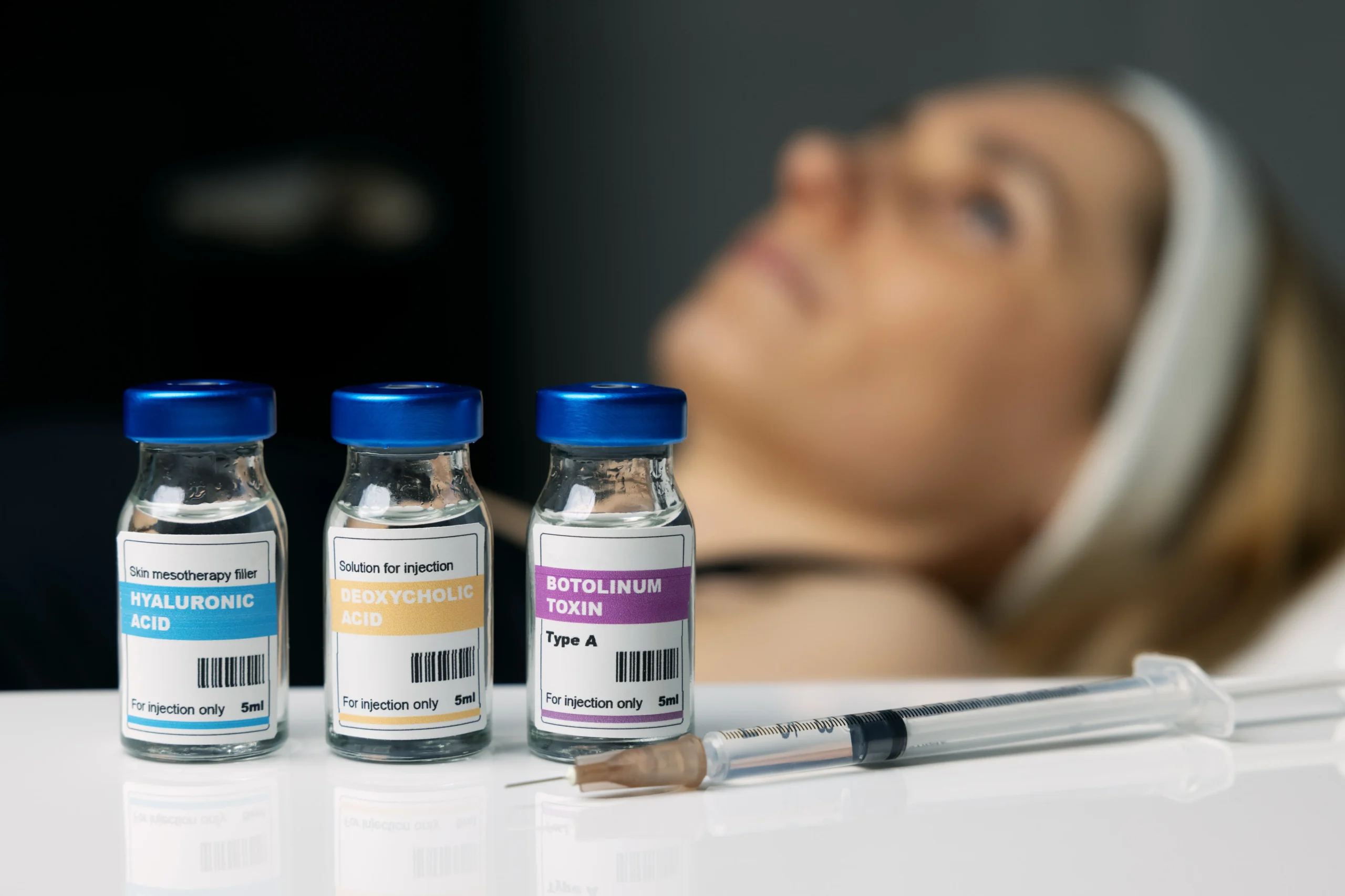 Three labeled injectable vials and a syringe on a counter with a person in the background